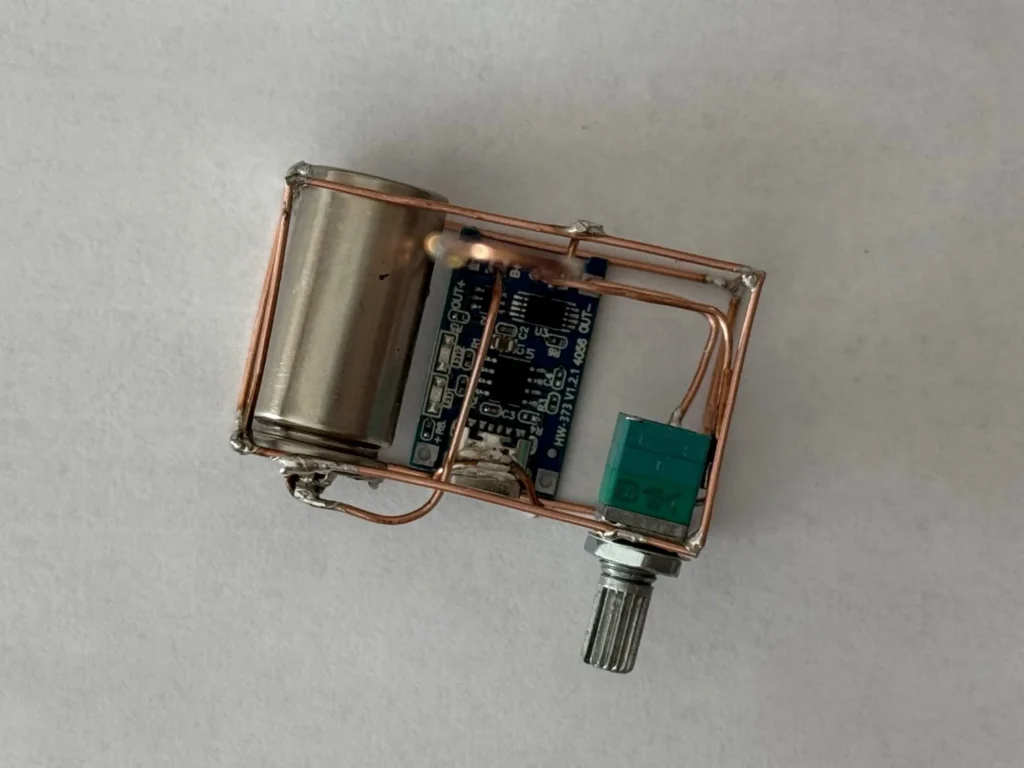 Top view of the soldered copper cage holding the 16340 cell, the blue TP4056 charger board and the green potentiometer