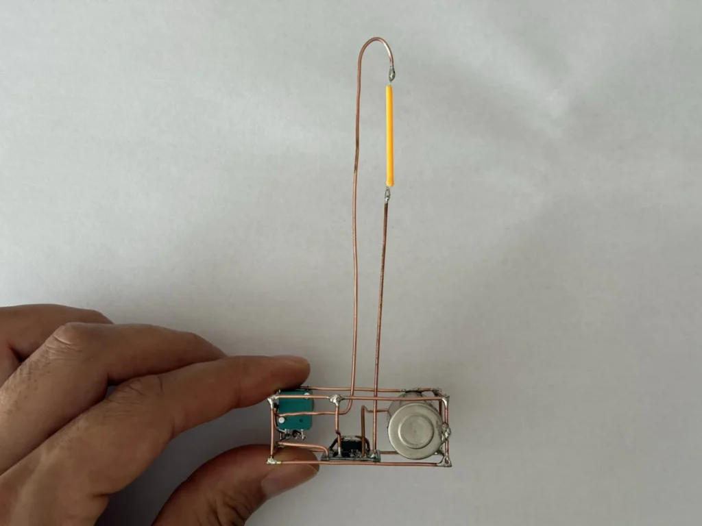Hand holding the finished copper wire lamp from the front, showing the battery, the USB-C port and the dimmer knob in the copper base