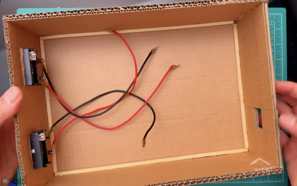 Inside of the cardboard case with wooden strips along the edges, the meters on the front wall and red and black wires from the binding posts