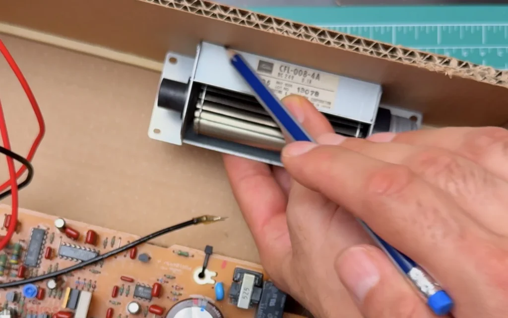 Marking the position of the salvaged Toshiba CFL-008-4A cross-flow fan against the side wall of the cardboard case with a pencil
