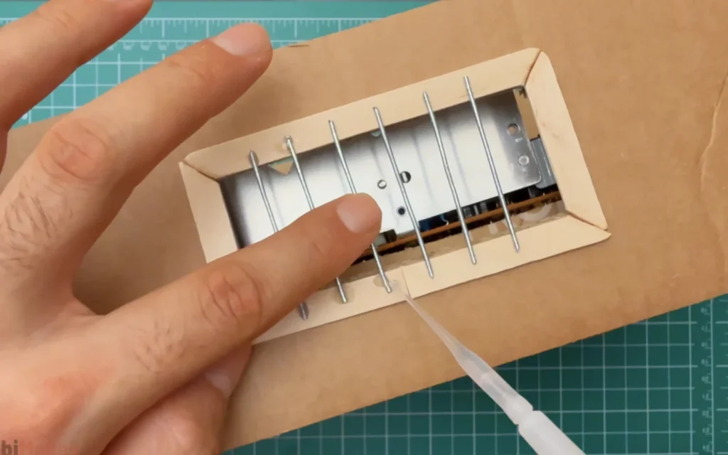 Gluing thin metal rods across a craft-stick framed vent opening in the cardboard case to make a ventilation grille
