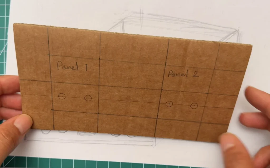 Cardboard front panel marked with a pencil grid, labelled Panel 1 and Panel 2, with circles for the binding posts