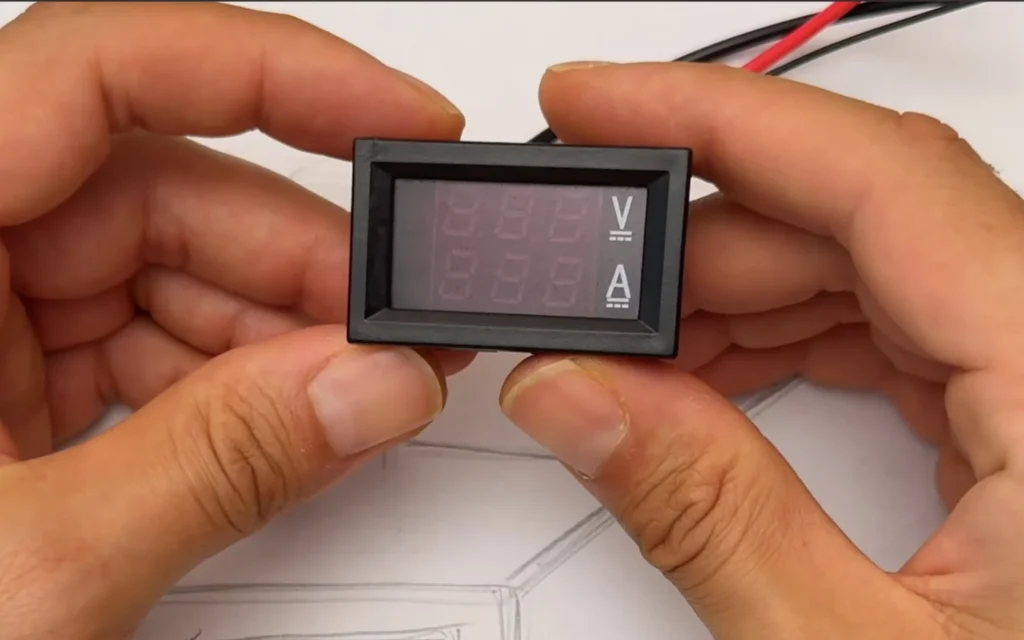 Hand holding a small dual digital voltmeter and ammeter module with V and A markings