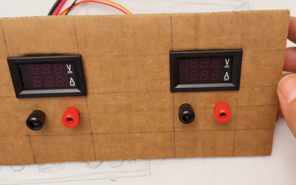 Cardboard front panel with two digital meters fitted and a black and red binding post under each one