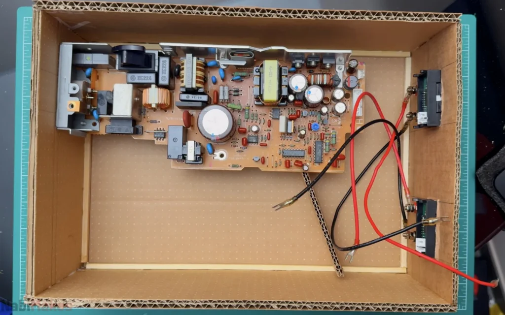 Printer power supply board placed inside the cardboard case, with the output wires running to the meters on the front panel