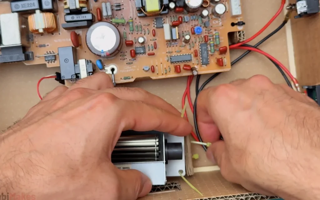 Tightening zip ties around the cross-flow fan to fix it inside the cardboard case next to the power supply board