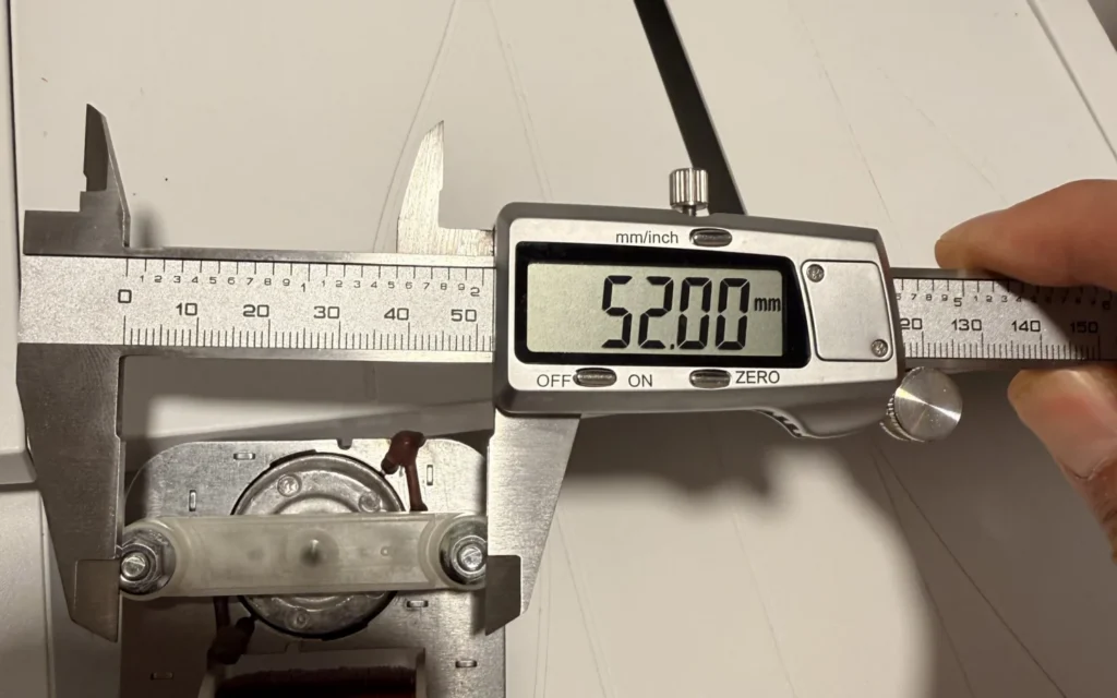 Digital calipers reading 52.00 mm across the mounting holes of the microwave fan motor's metal frame