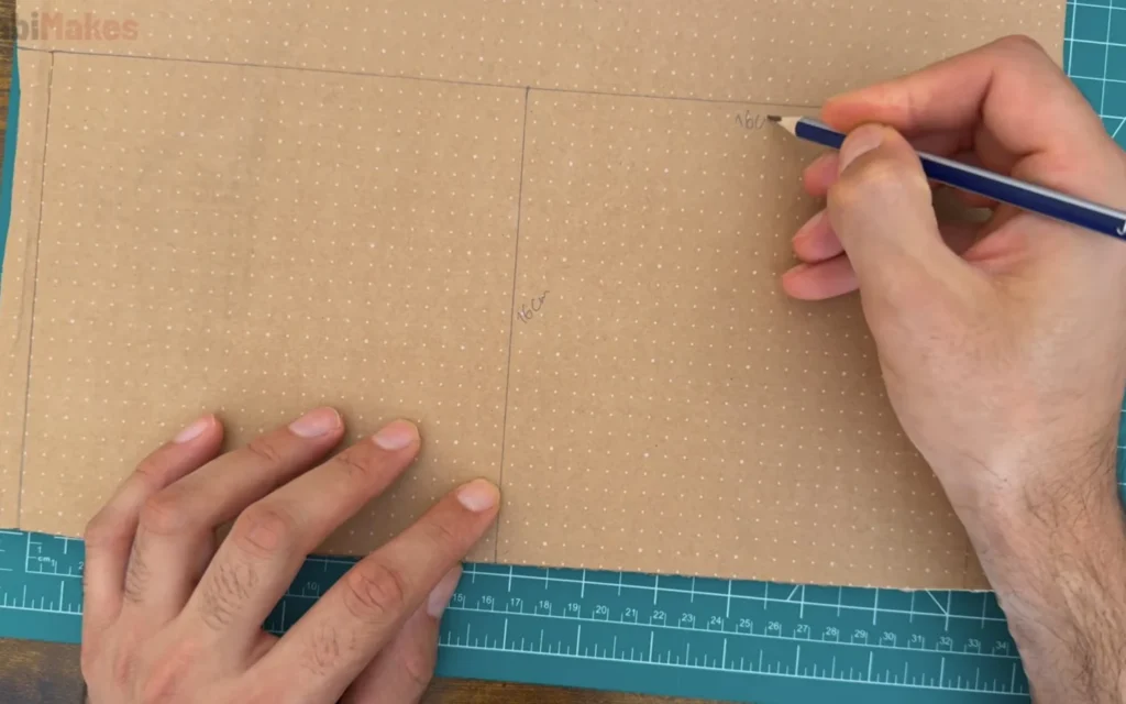Hand marking 16 cm lines on a sheet of cardboard with a pencil on a green cutting mat