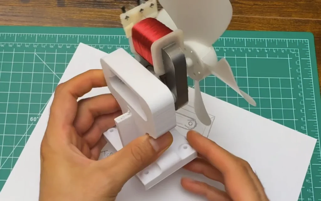 The microwave fan motor screwed onto the stronger white 3D-printed mount, held over the paper sketch