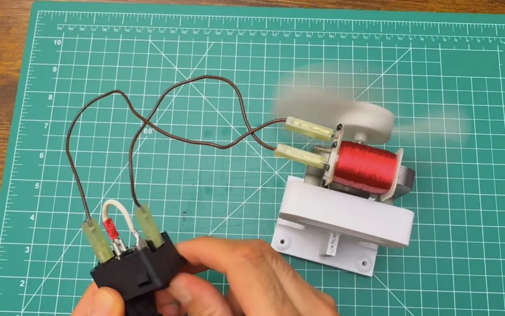 The wired power inlet module connected to the microwave fan motor on its mount, the blade blurred as it spins