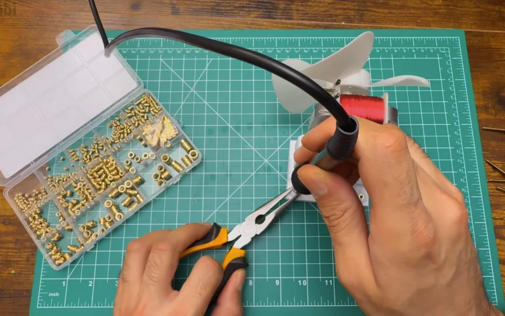 A soldering iron pressing a brass heat-set insert into the printed motor mount, next to a box of assorted inserts