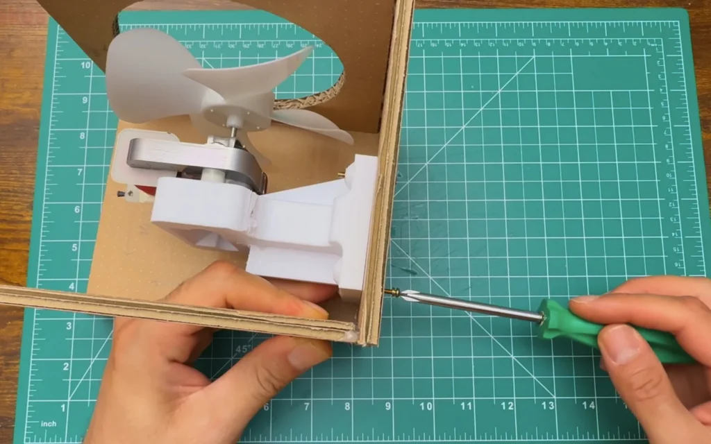 Screwdriver tightening a screw through the cardboard bottom panel into the printed motor mount inside the box