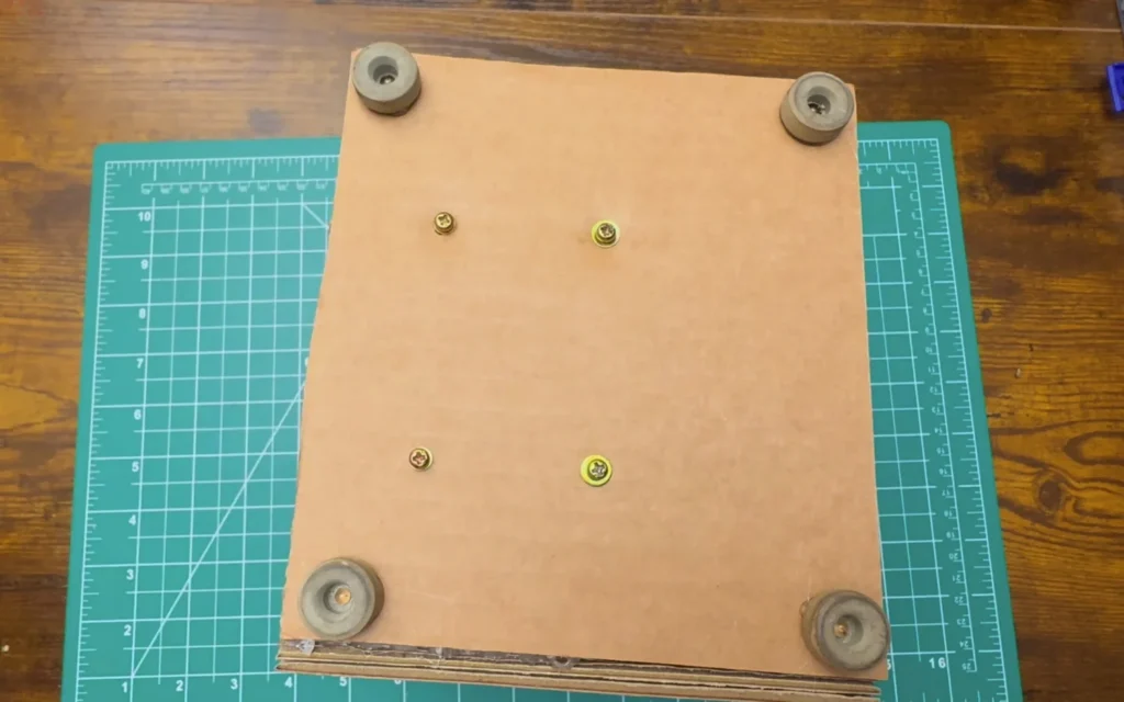 Bottom of the cardboard fan with four rubber feet in the corners and four screws with washers holding the motor mount