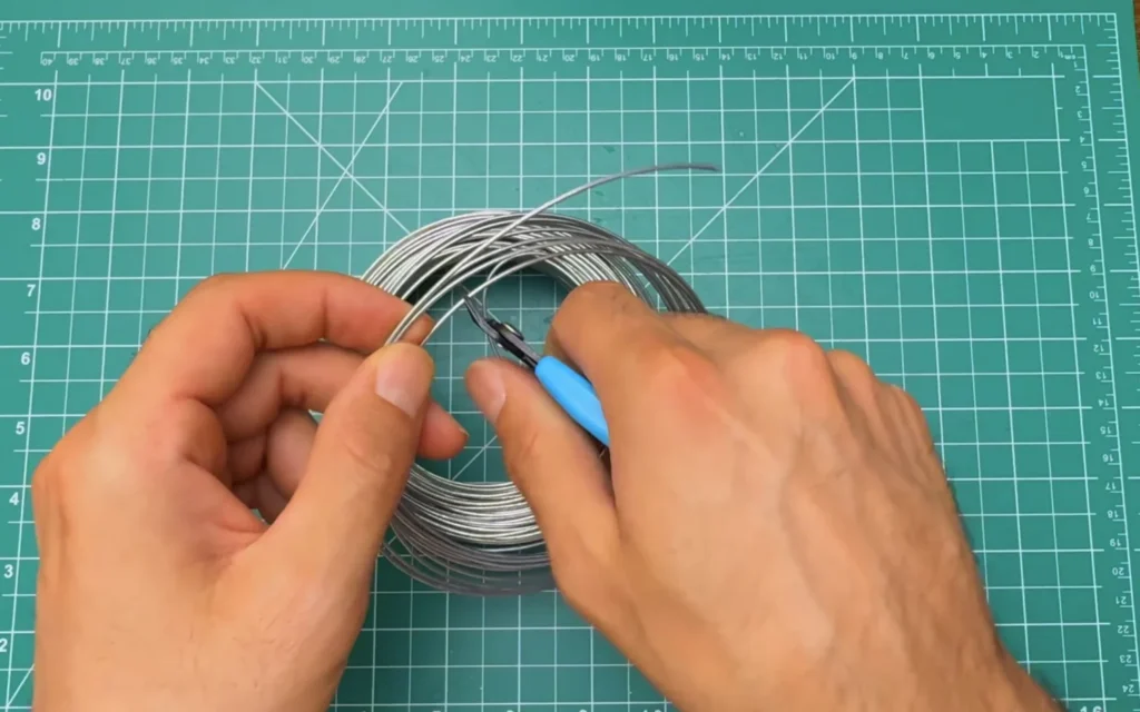 Hands cutting a length of stainless steel wire from a coil with blue-handled wire cutters