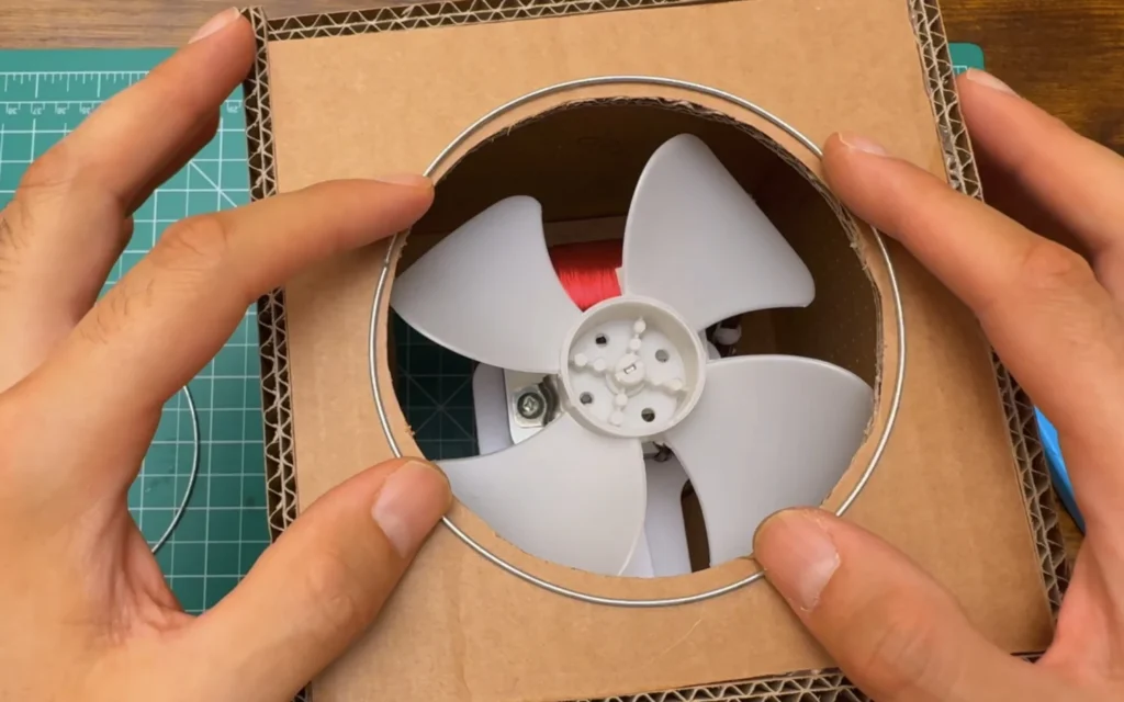 A stainless steel wire ring held on the cardboard front panel around the round fan opening