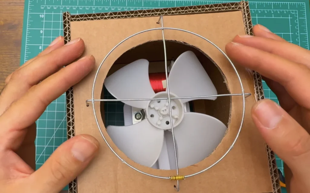 The wire ring and cross hooked into the front panel of the fan, in front of the white blade