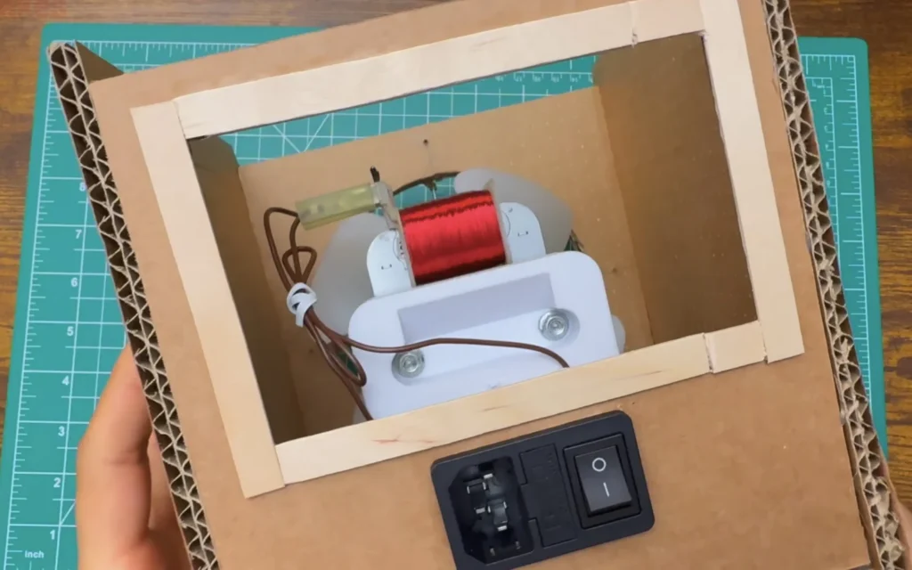 Back panel of the cardboard fan with a frame of wooden craft sticks around the rectangular opening and the power inlet module below