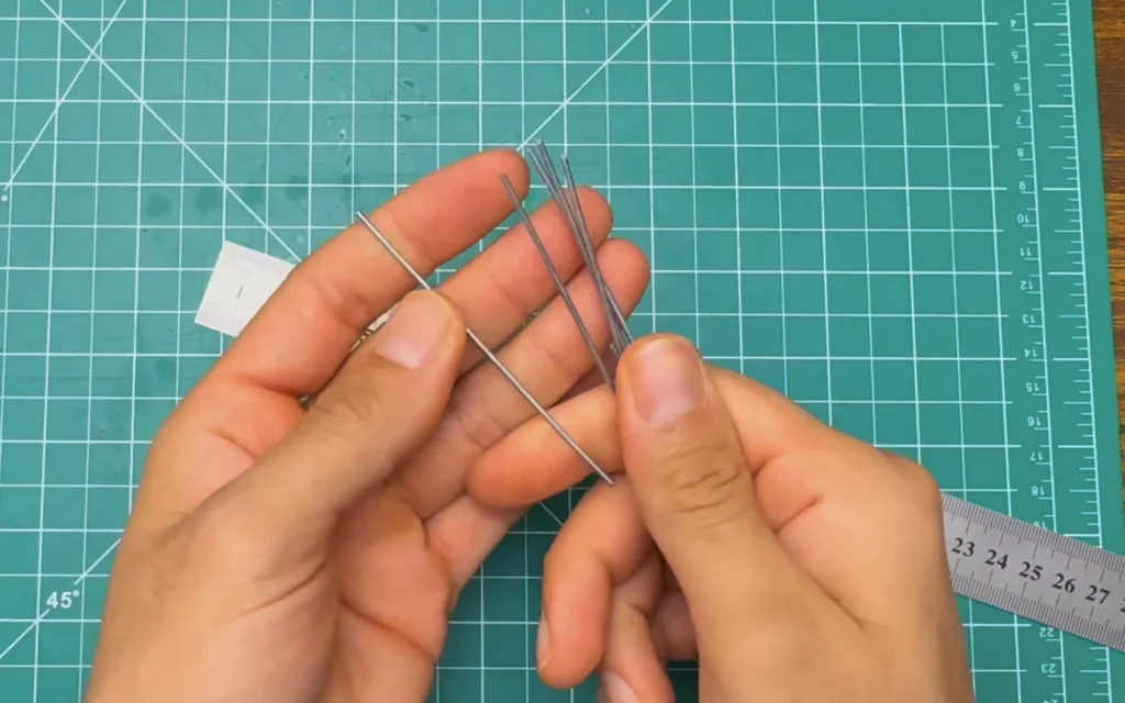 Hands holding several short straight stainless steel rods cut for the back grille