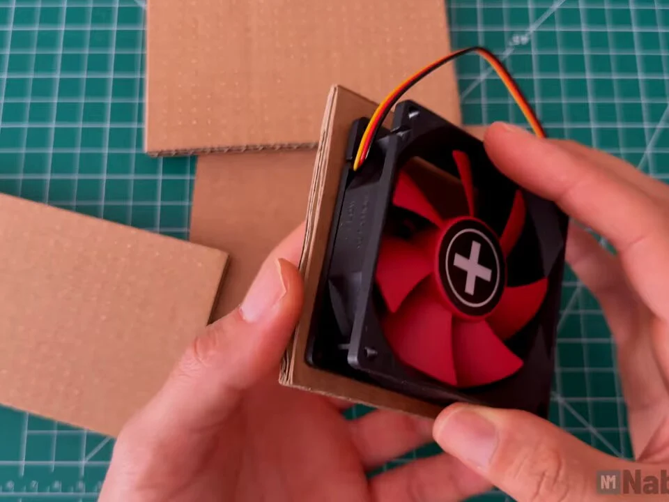 Red and black 80 mm PC fan held on a cardboard panel to trace the opening