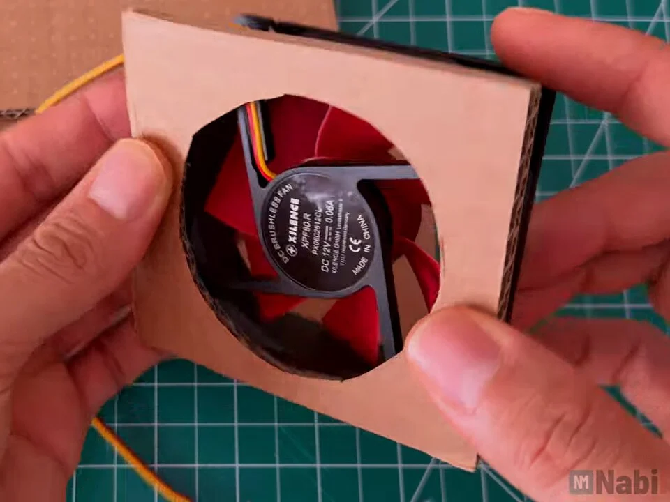 Fan held behind the round opening cut in the cardboard front panel