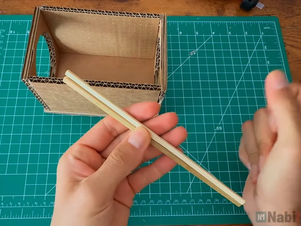 Long thin square wooden stick held next to the open cardboard box