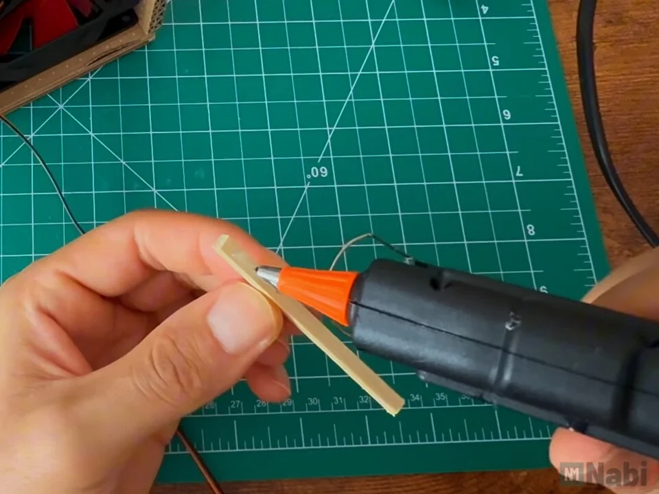Hot glue gun applying glue to a short wooden stick