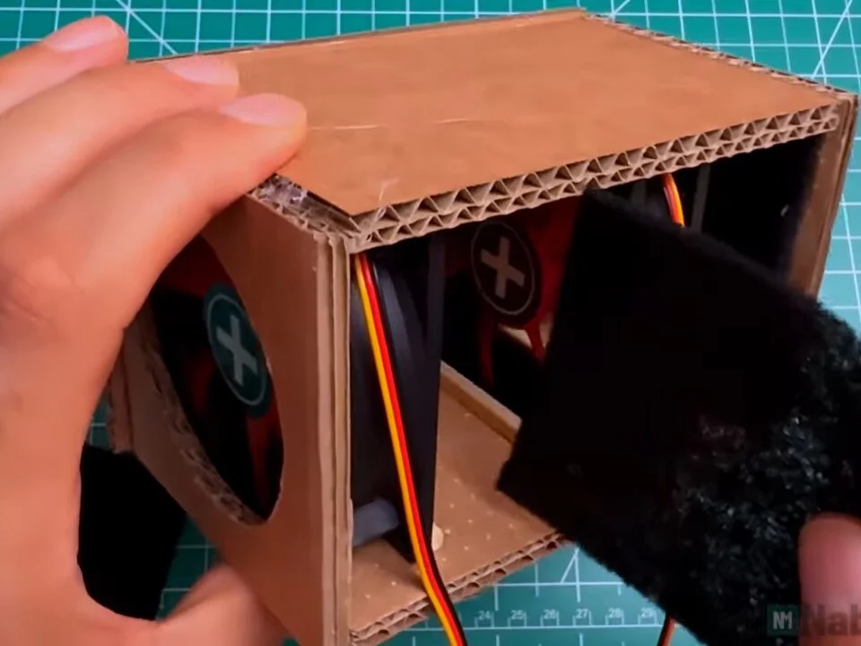 Stack of carbon filter squares being pushed into the back of the box behind the second fan