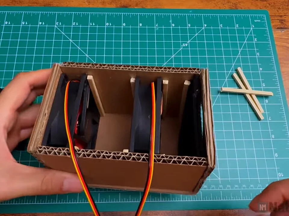 Open box with three compartments separated by wooden stick stops: two fans and the filter