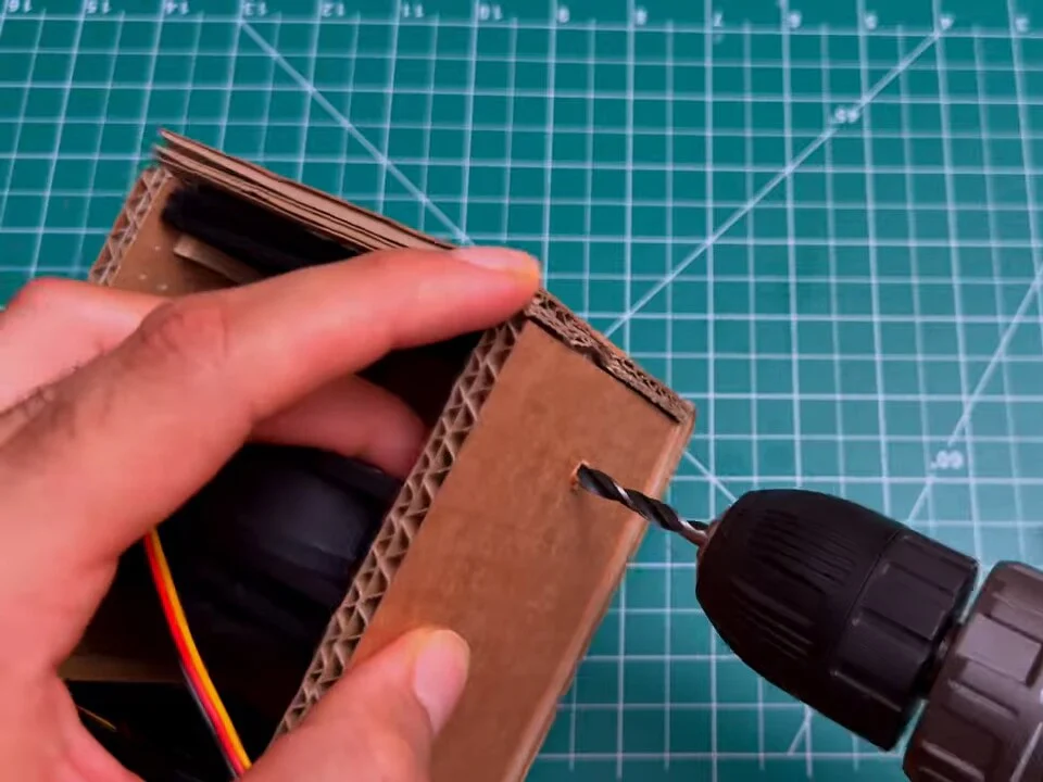 Cordless drill making a hole in the side of the cardboard box for the switch
