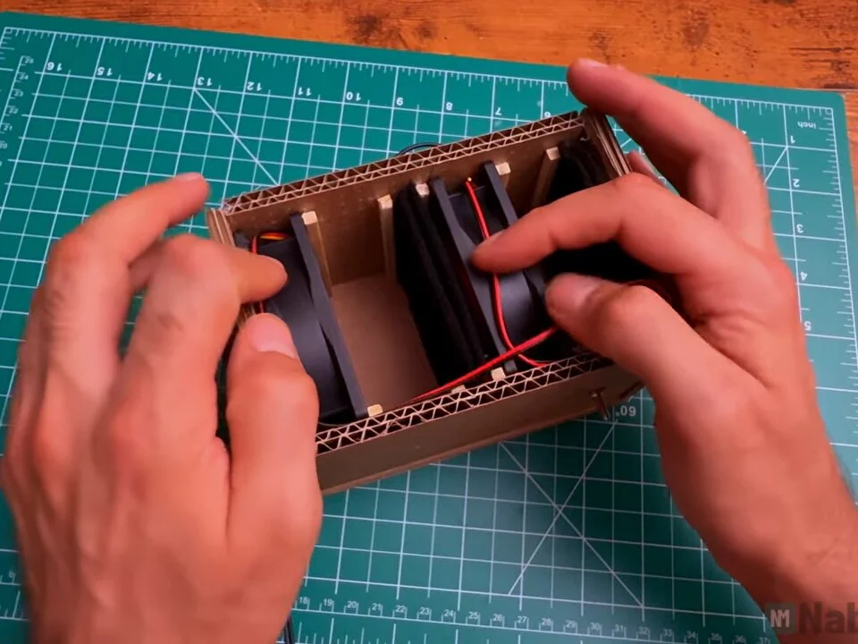 Hands tucking fan wires along the inside walls of the box