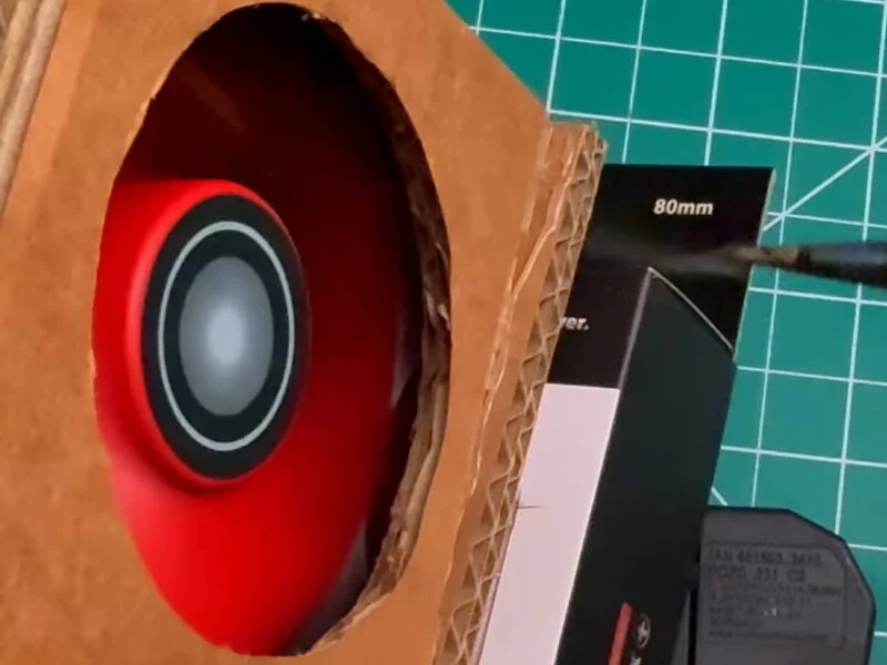 Red fan running behind the round cardboard opening while a soldering iron tip beside it releases a thin trail of smoke
