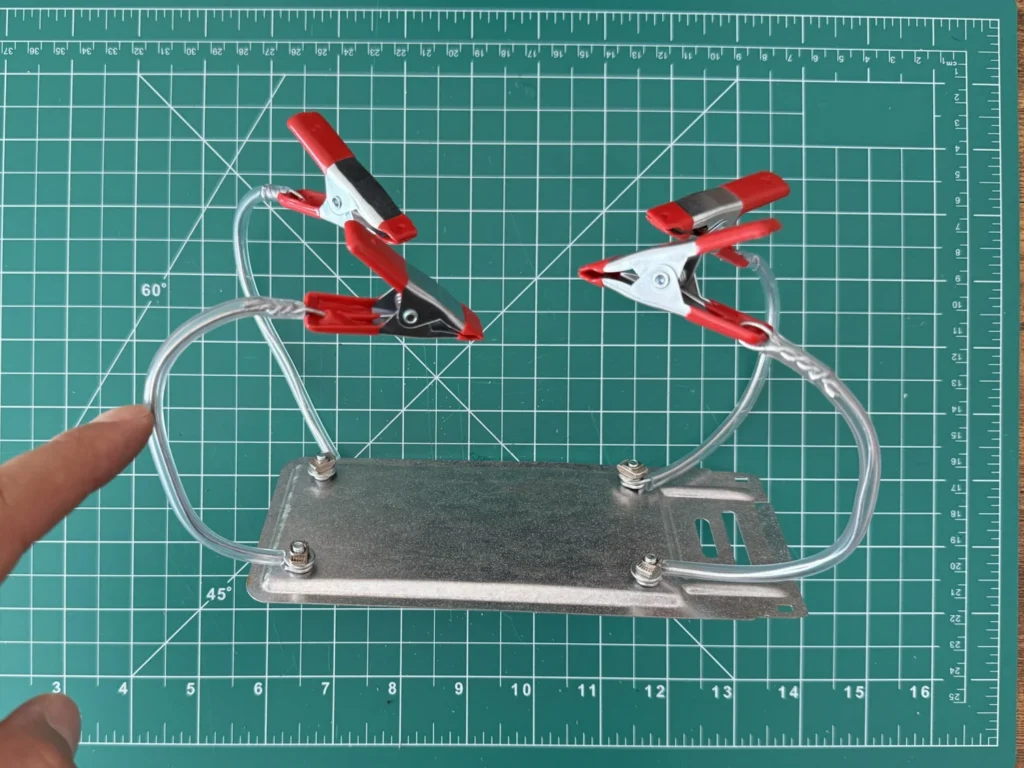 A finger pointing at one of the looped wire arms of the DIY helping hands while the clips are being positioned