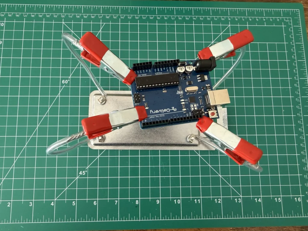 Top view of an Arduino Uno held by the four red clips of the DIY helping hands above the metal base