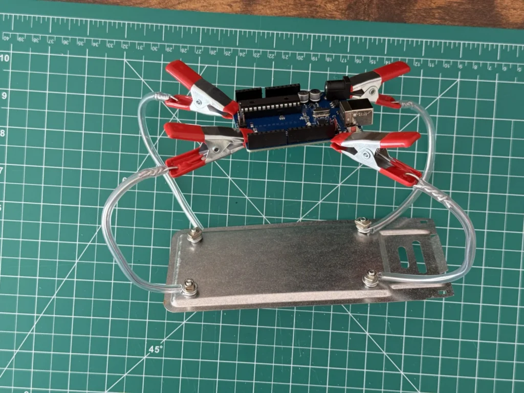 Side view of the DIY helping hands with an Arduino Uno held above the base plate by four clips on looped wire arms