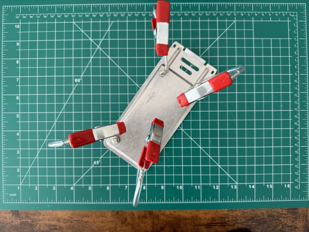 Top view of the metal base plate on the cutting mat with wire arms and red clips attached near its corners
