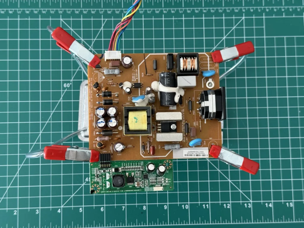 A large power-supply circuit board held flat by the four clips of the DIY helping hands