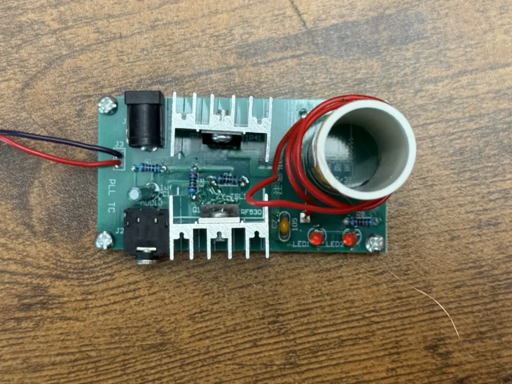 Top view of the assembled Tesla coil board with the TIP41 and IRF530 screwed to aluminium heatsinks, the jacks, LEDs and the coil in place
