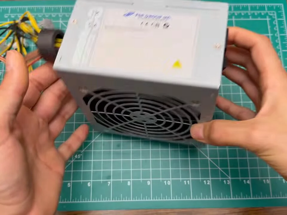 Old silver ATX PC power supply with cut, re-used wires held over a cutting mat