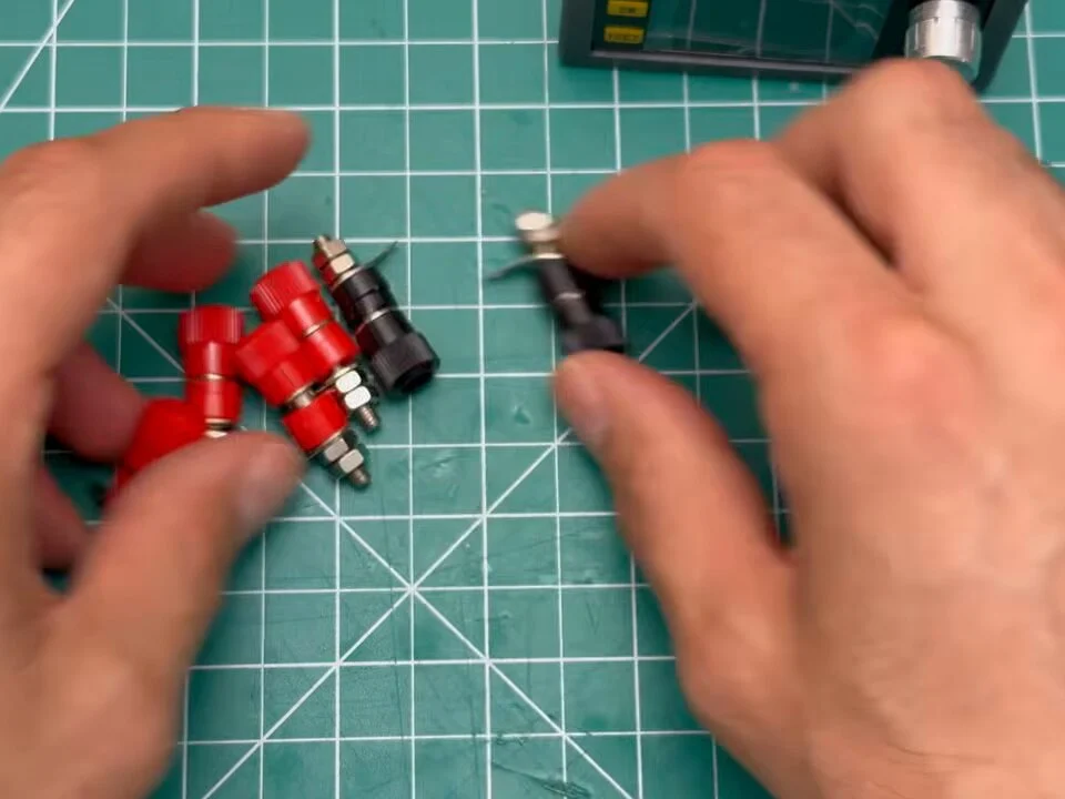 Red and black 4 mm banana jacks and a black rocker switch on the cutting mat