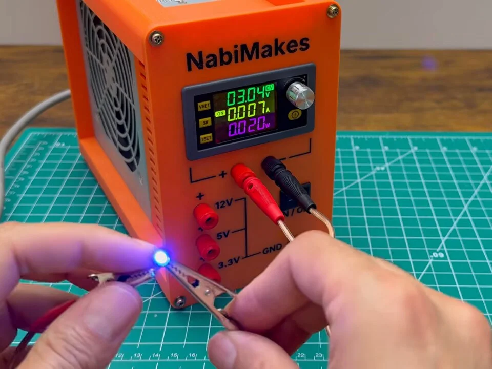 Small blue LED lit from the variable output, held in crocodile clips in front of the power supply