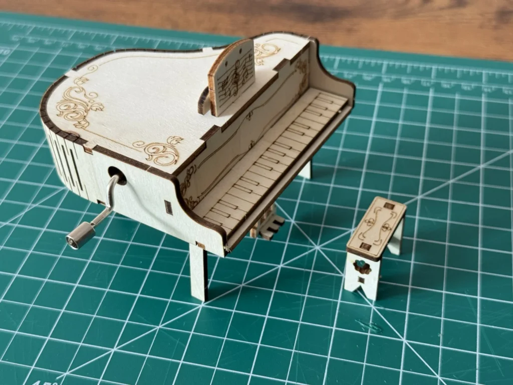 The finished wooden piano seen from above, showing the curved side wall with its living-hinge cuts and the crank on the side