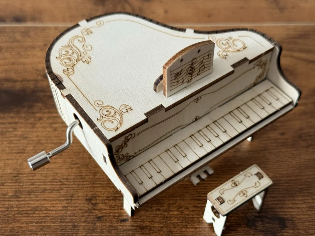 Close-up of the wooden piano music box from above, showing the engraved lid decorations, the music stand and the laser-cut keys