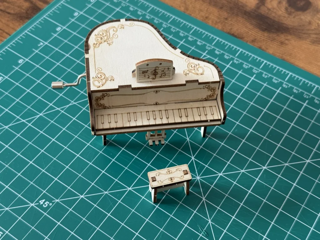 Front view of the wooden piano music box showing the engraved keyboard, the lid and the little music stand