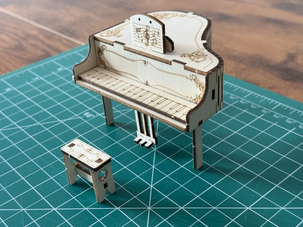 The wooden piano standing on its legs with the pedal piece underneath and the small bench in front, on a green cutting mat